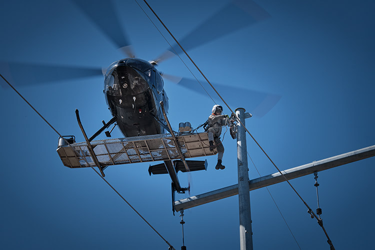 A man working on top of a power line while being suspended by a helicopter.