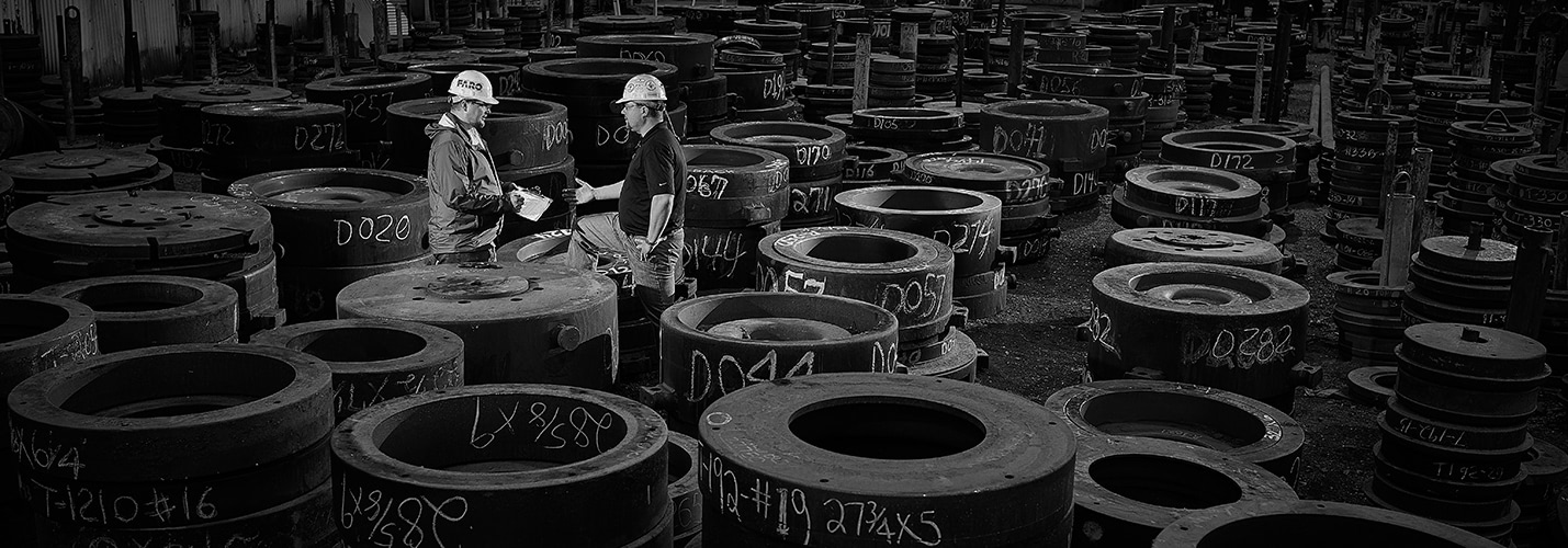 Black and white photo of two men in a warehouse surrounded by steel cylinders.