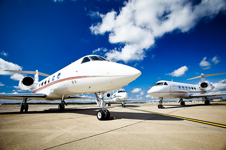 A low angle shot of two private jets on a runway with a bright blue sky behind them.