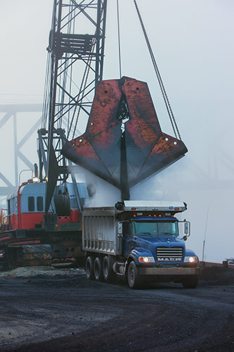 A giant crane dumping coal into a large dump truck.