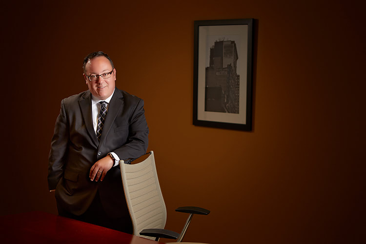 Portrait of a man in a suit with his arm on the back of a chair.