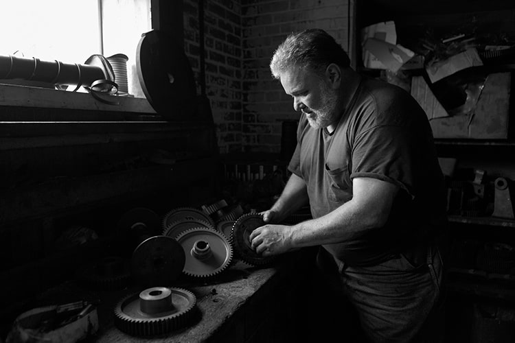 Black and white portrait of a man working on gears at a bench.